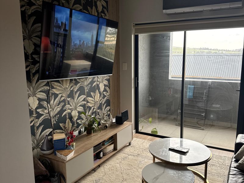 A well-maintained living room featuring a decorative wallpaper accent wall, split-system air conditioning, and direct access to a private balcony through sliding glass doors.