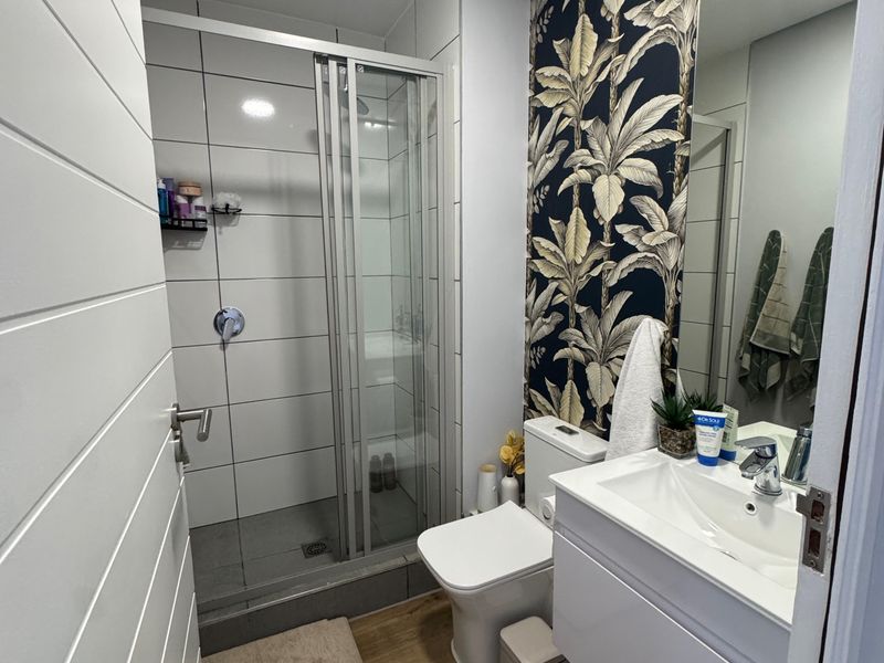 A modern bathroom featuring a glass-enclosed shower, a vanity basin with storage, and a decorative feature wall with tropical wallpaper.