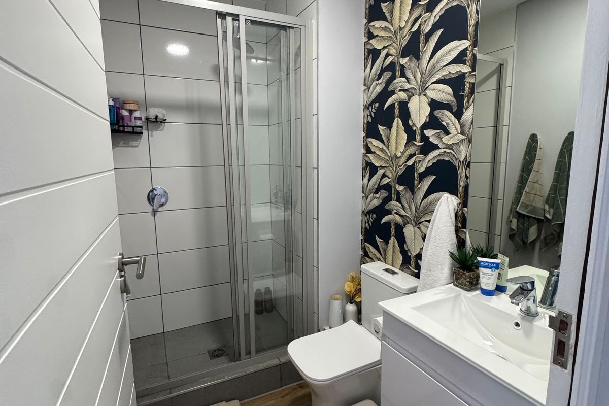 A modern bathroom featuring a glass-enclosed shower, a vanity basin with storage, and a decorative feature wall with tropical wallpaper.