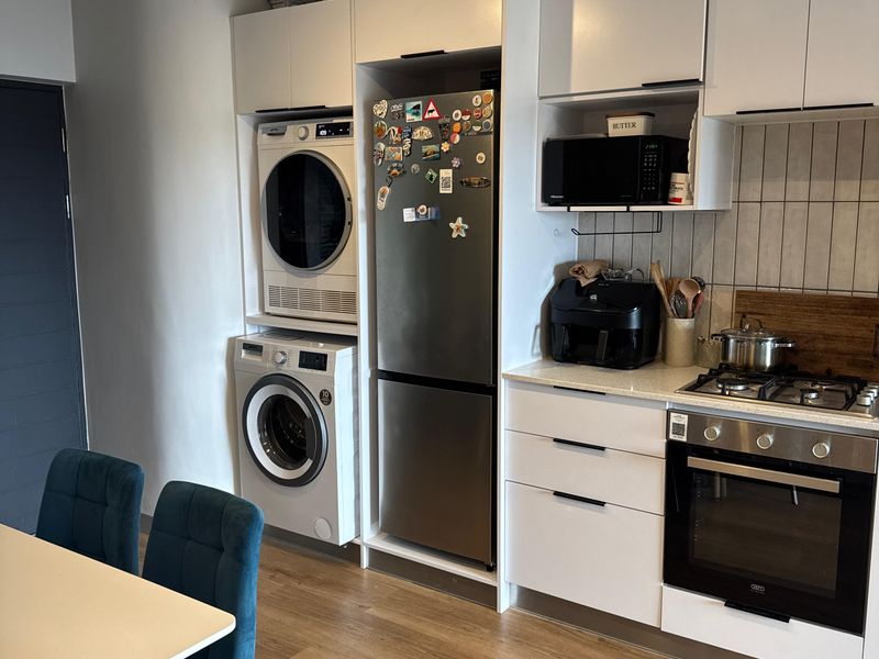 Modern open-plan kitchen featuring integrated laundry appliances, sleek white cabinetry, gas hob, built-in oven, and durable laminate flooring.
