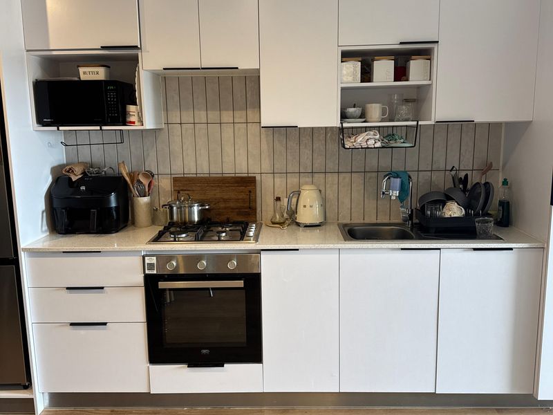 Modern kitchen featuring white cabinetry, stone countertops, a gas hob, built-in oven, and a tiled backsplash, complemented by durable laminate flooring.