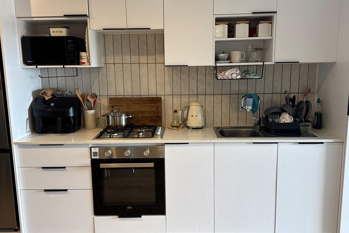 Modern kitchen featuring white cabinetry, stone countertops, a gas hob, built-in oven, and a tiled backsplash, complemented by durable laminate flooring.