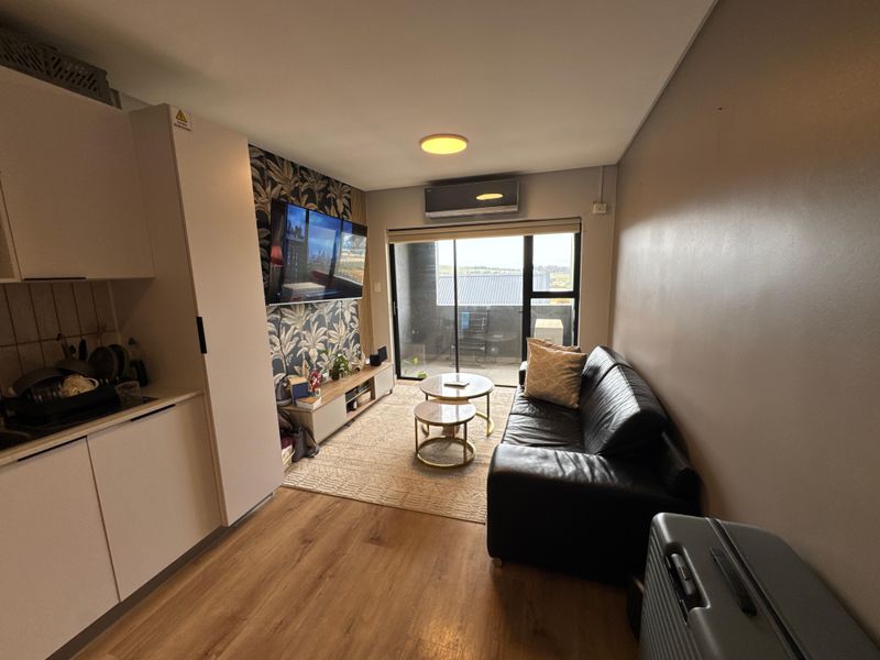 Modern open-plan living area featuring laminate flooring, a split-system air conditioner, and direct access to a private balcony through sliding glass doors.