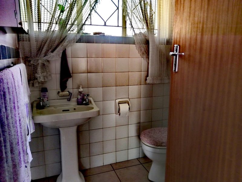A compact bathroom featuring a pedestal basin, toilet, and tiled finishes, requiring cosmetic updates to modernize the space.