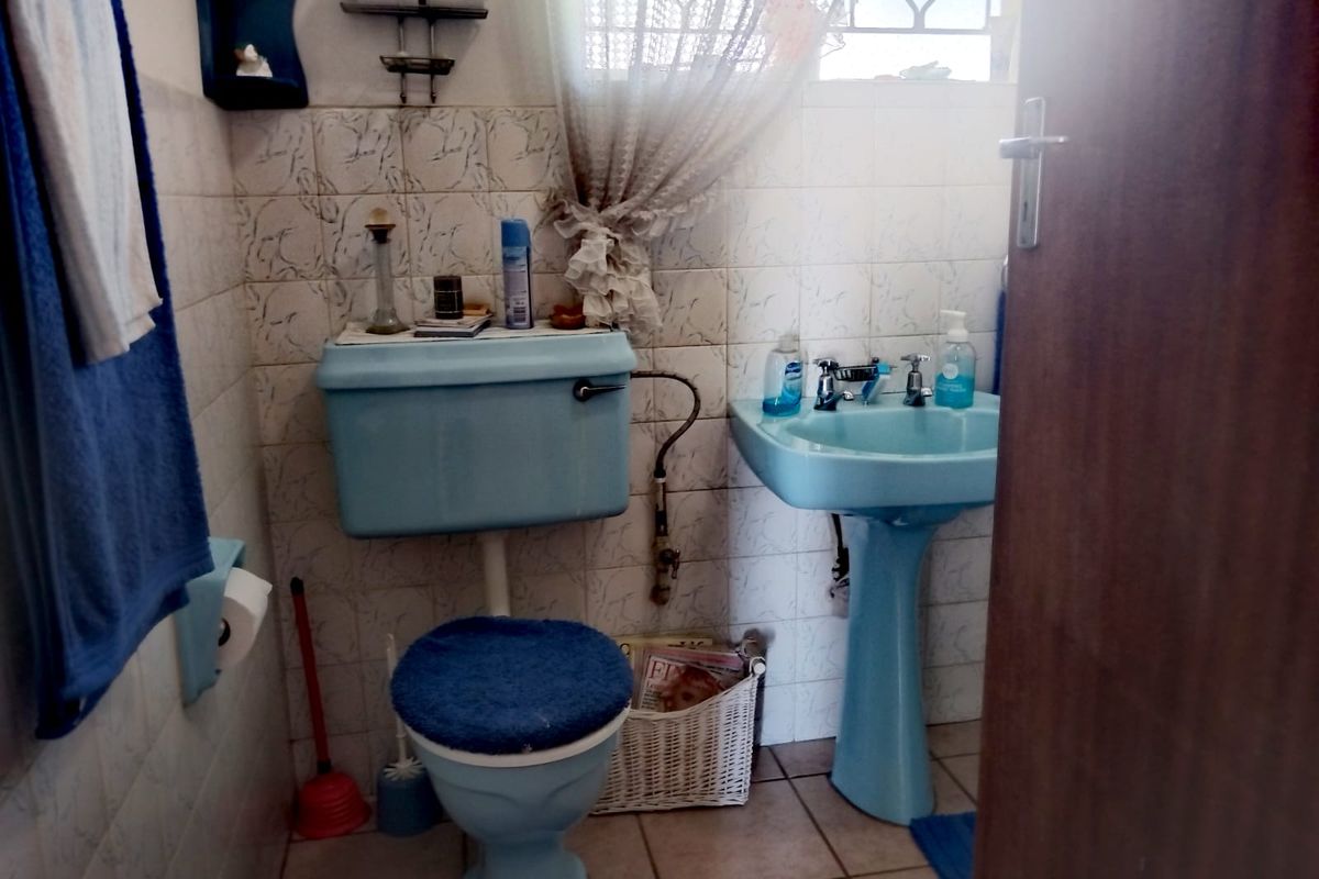 A compact bathroom featuring dated blue sanitaryware, including a pedestal basin and toilet, with tiled walls and floors.