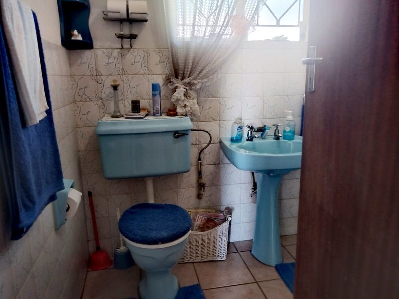 A compact bathroom featuring dated blue sanitaryware, including a pedestal basin and toilet, with tiled walls and floors.