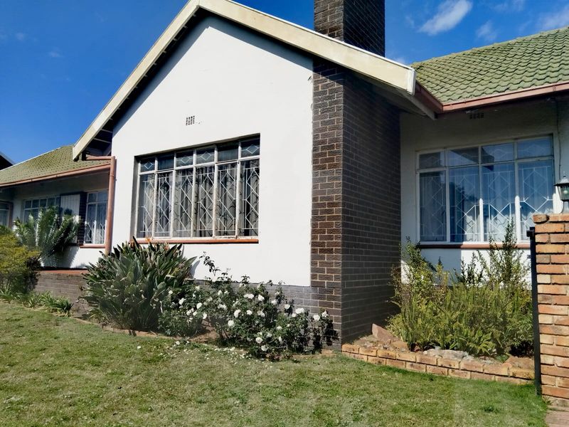 Front elevation of a single-story house featuring a brick chimney, tiled roof, and security-barred windows set within a landscaped garden.
