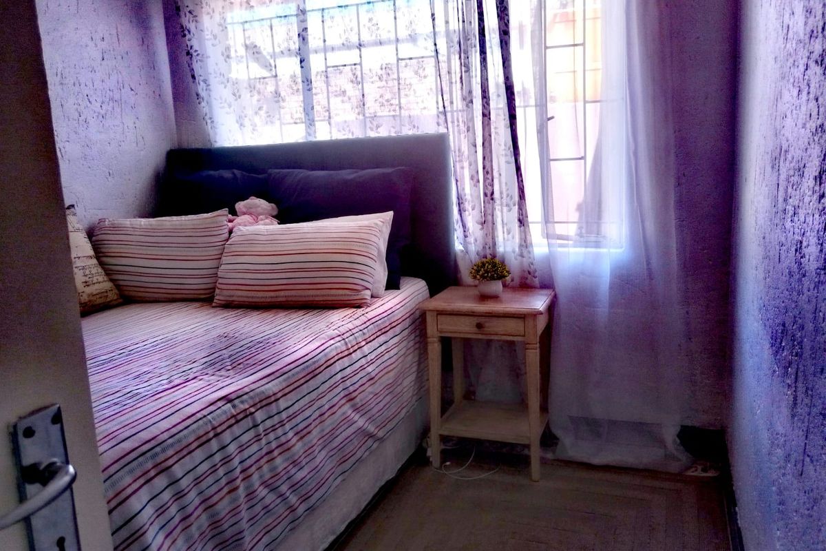 A compact bedroom featuring a window with security bars and textured wall finishes.