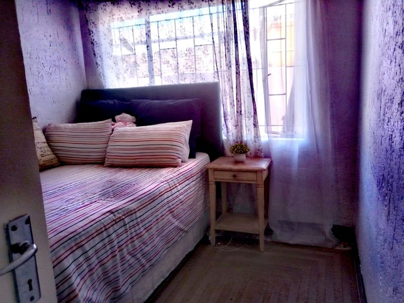 A compact bedroom featuring a window with security bars and textured wall finishes.