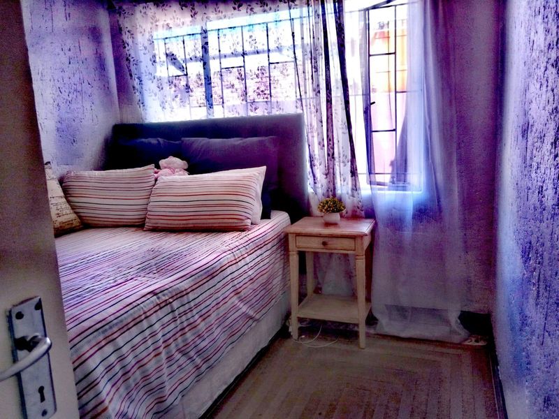 A compact bedroom featuring a window with security bars and textured walls in need of maintenance.
