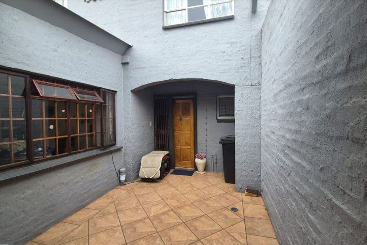 A private rear courtyard featuring tiled flooring, textured masonry walls, and a timber entrance door with security gate access.