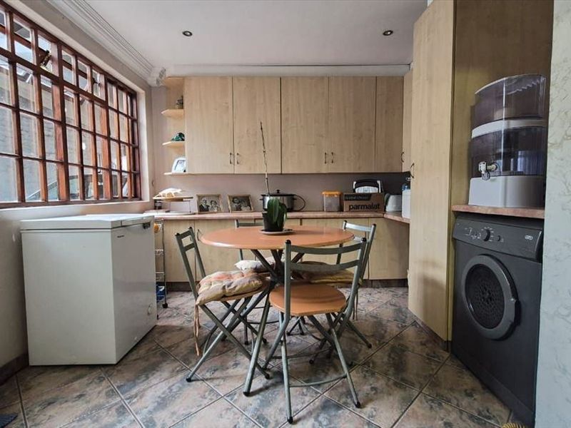 A functional kitchen featuring light-toned built-in cabinetry, tiled flooring, and a large timber-framed window providing natural light.