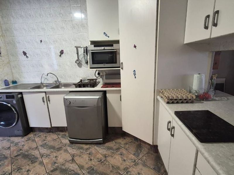 A functional kitchen featuring built-in cabinetry, laminate countertops, a stainless steel sink, and tiled finishes, offering potential for a modern renovation.