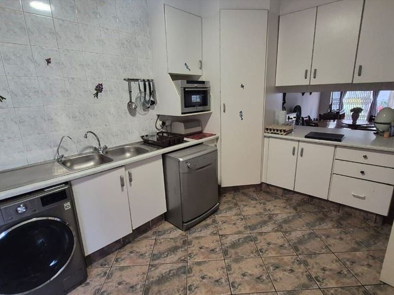 A functional kitchen featuring built-in cabinetry, laminate countertops, a stainless steel sink, and tiled finishes, offering a practical layout for daily use.