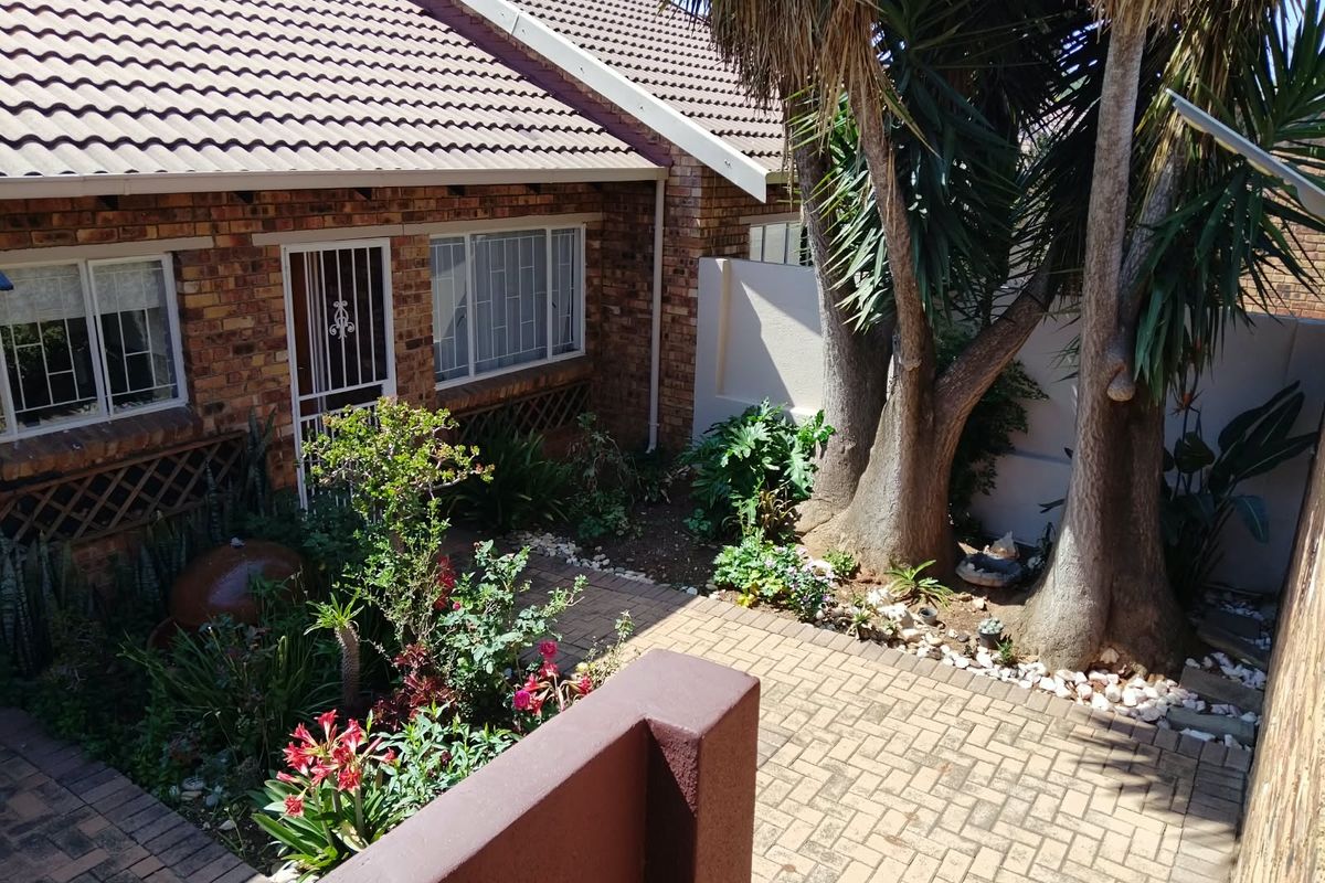 A private rear courtyard featuring brick paving, established trees, and direct access to the townhouse interior through a security gate.