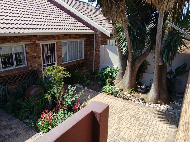A private rear courtyard featuring brick paving, established trees, and direct access to the townhouse interior through a security gate.