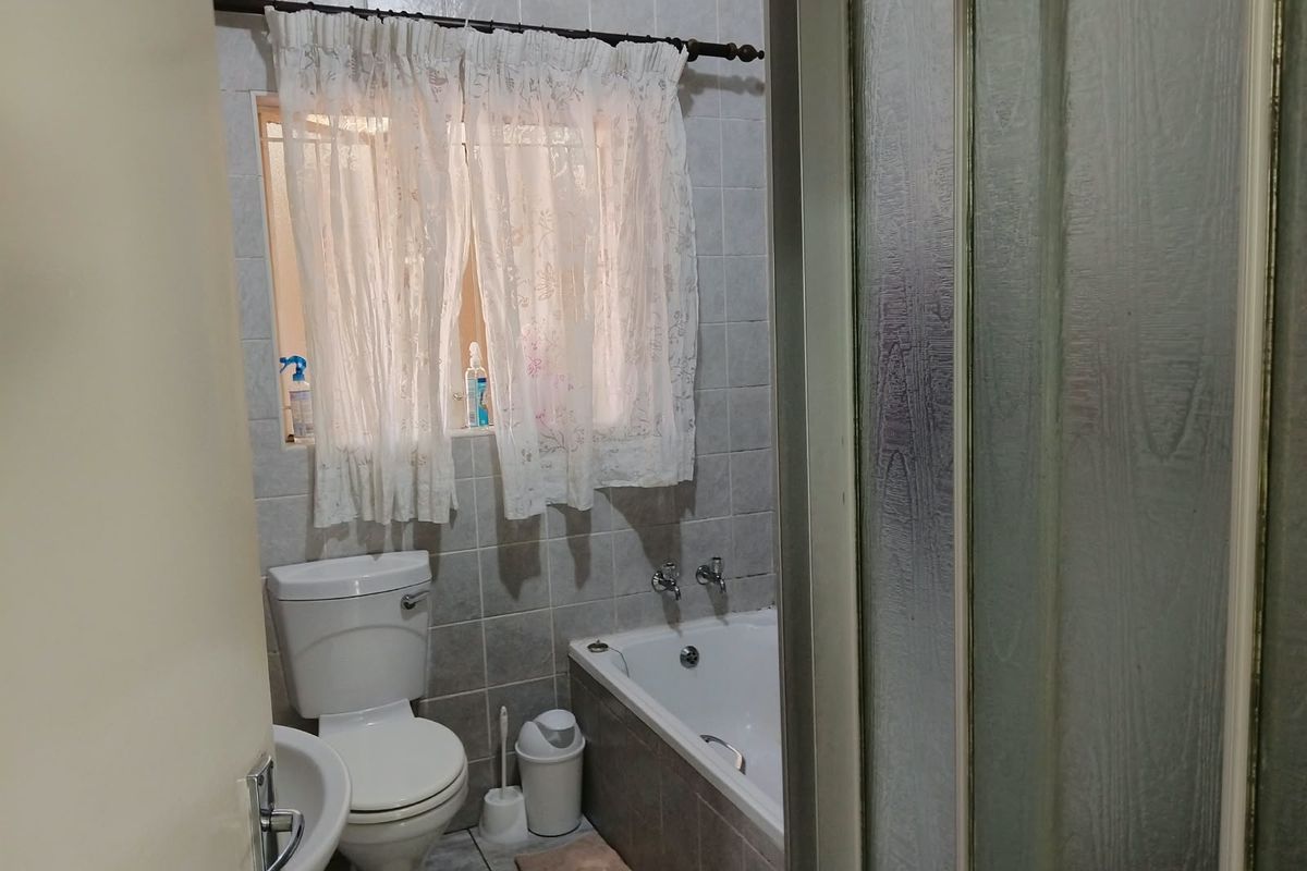 A functional bathroom featuring a bathtub, toilet, and tiled finishes, offering a practical layout ready for potential cosmetic updates.