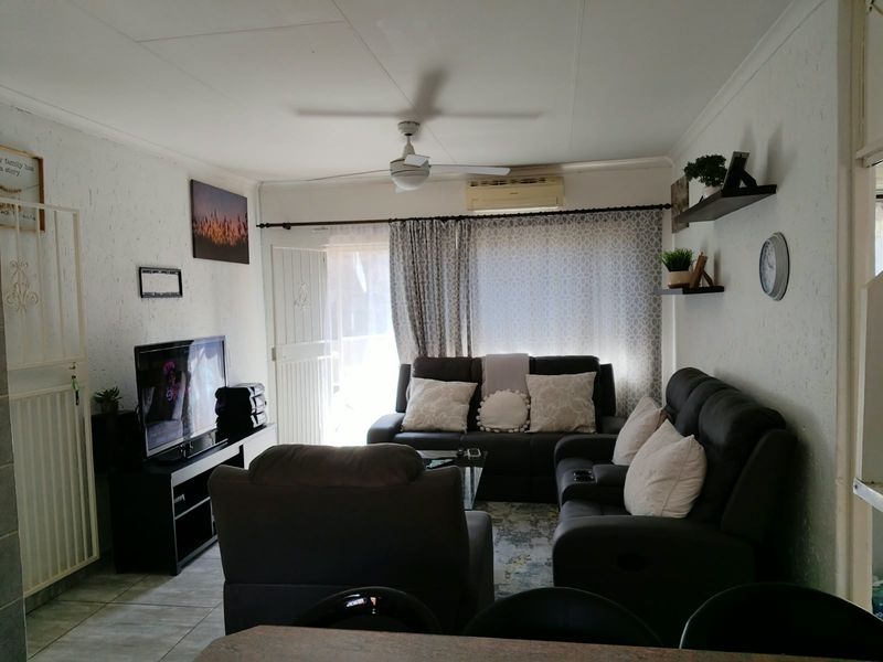 A comfortable living room featuring tiled flooring, a ceiling fan, and a wall-mounted air conditioning unit, providing a functional and climate-controlled space.