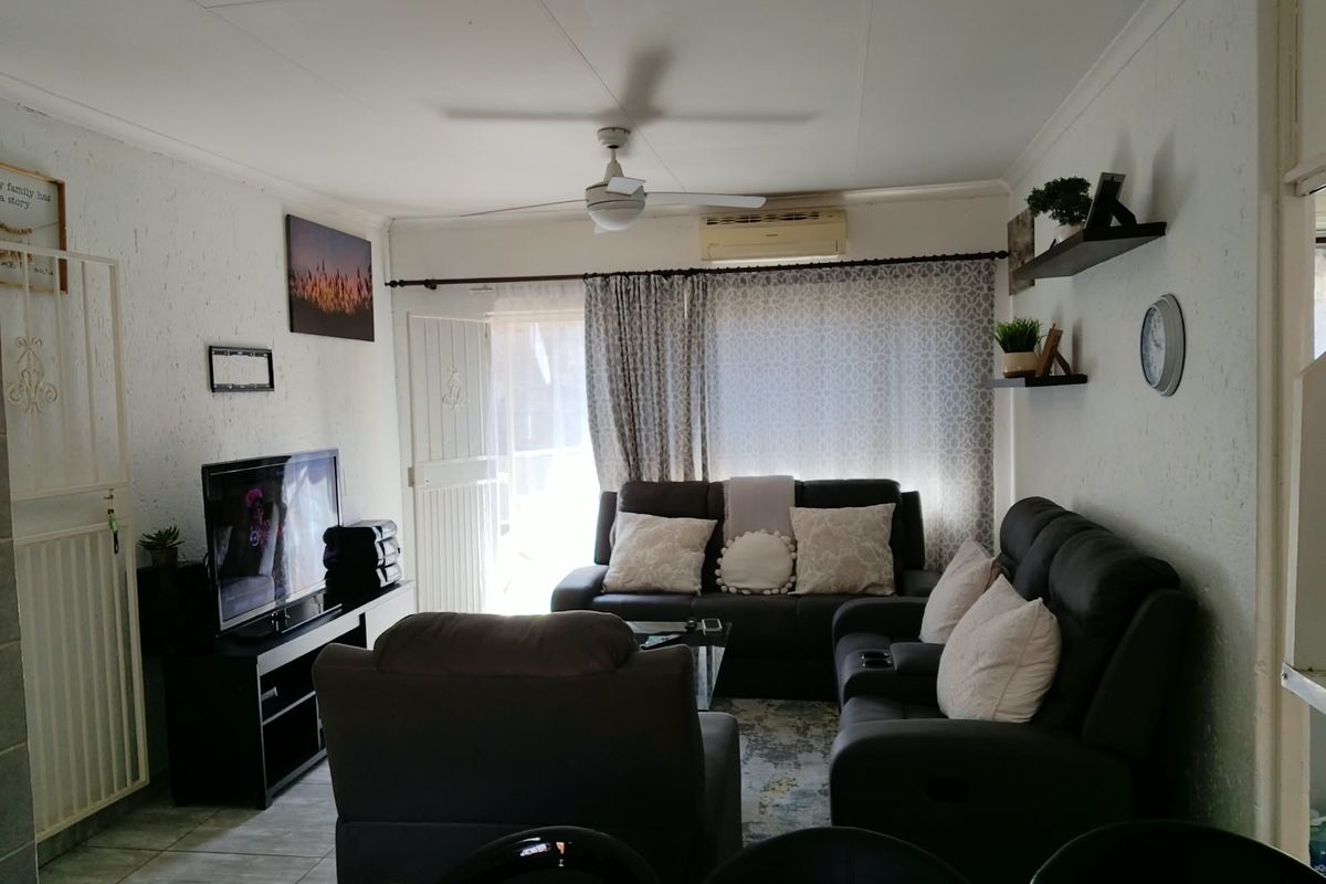 A comfortable living room featuring tiled flooring, a ceiling fan, and a wall-mounted air conditioning unit, providing a functional and climate-controlled space.