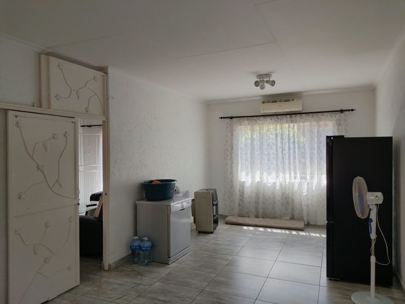Open-plan living area featuring tiled flooring, a wall-mounted air conditioning unit, and decorative security door access.
