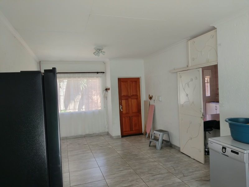 An open-plan living area featuring neutral tiled flooring, a solid wood entrance door, and a decorative security gate leading to the kitchen area.