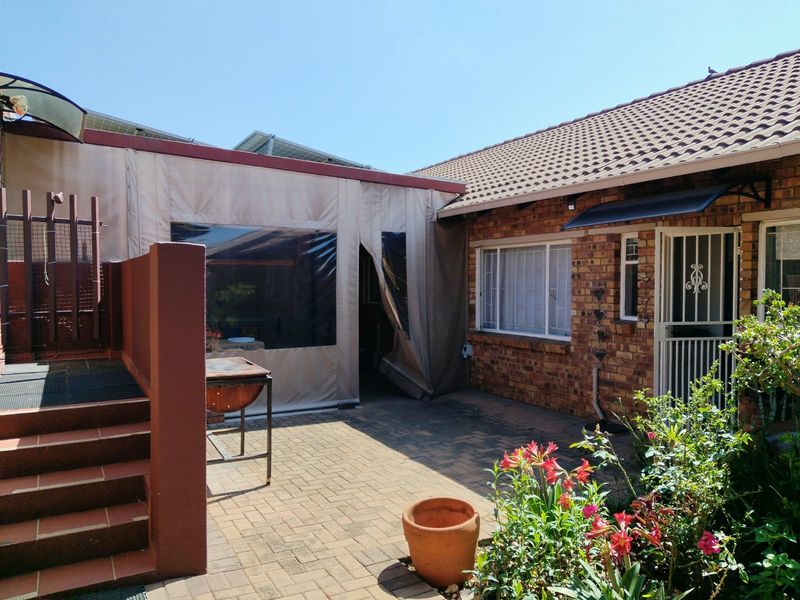 A paved outdoor patio area featuring a brick facade, security gate, and a protective canvas enclosure, offering a functional space for outdoor living.