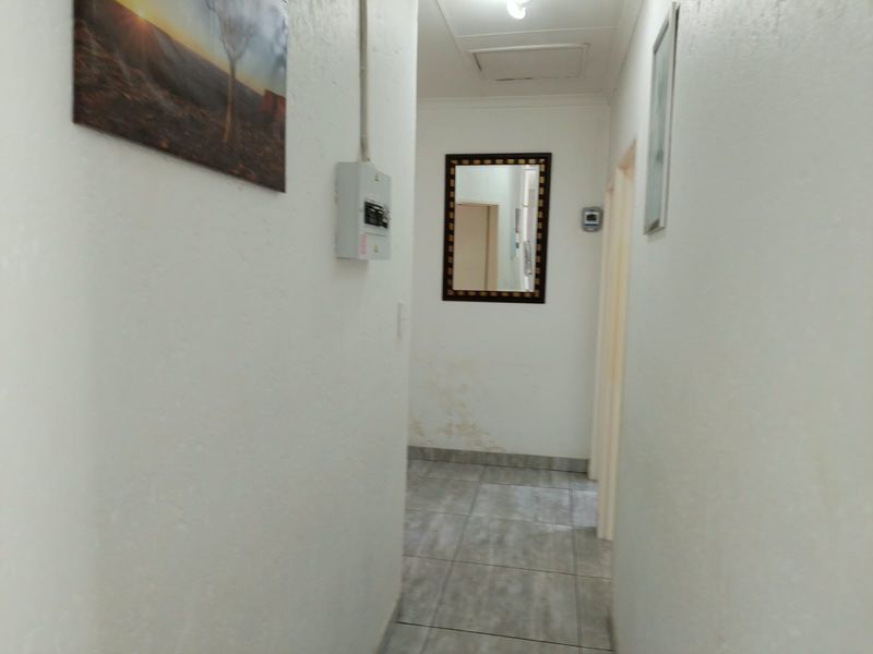A narrow hallway featuring tiled flooring and a ceiling access hatch, showing signs of wall moisture damage requiring maintenance.
