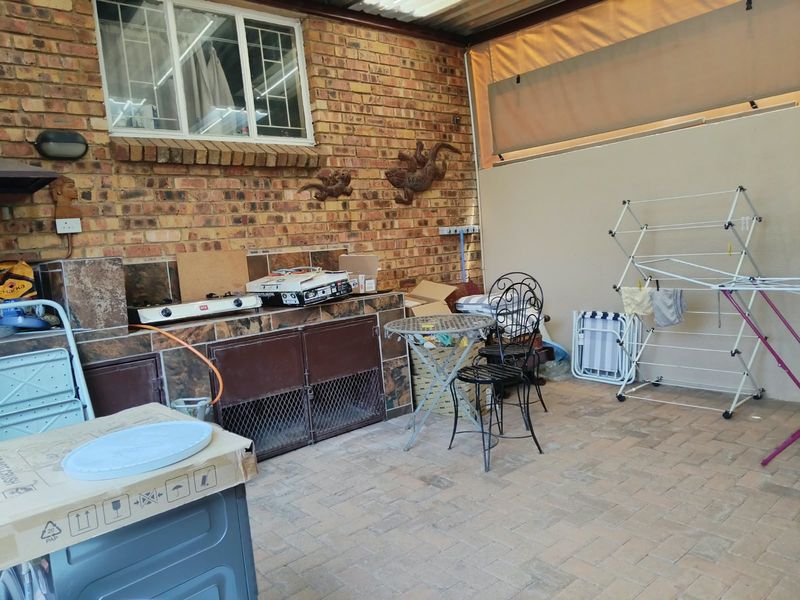 Covered patio area featuring a built-in braai with tiled counter space, brick wall finish, and paved flooring, suitable for outdoor entertainment.