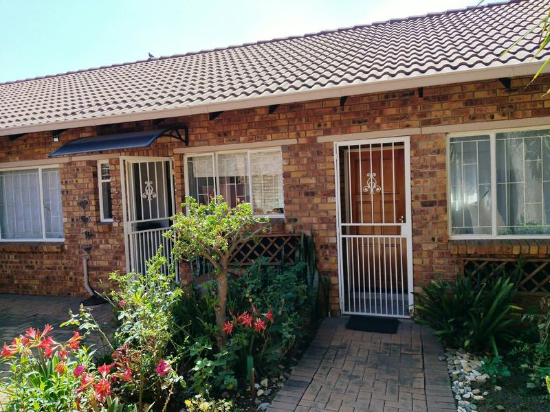 Front facade of a face brick townhouse featuring a paved entrance path, security gates, and well-maintained garden beds.