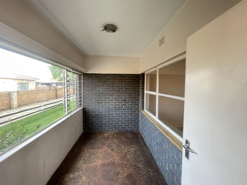 An enclosed balcony or sunroom featuring stone flooring, exposed brick accents, and large windows providing natural light.