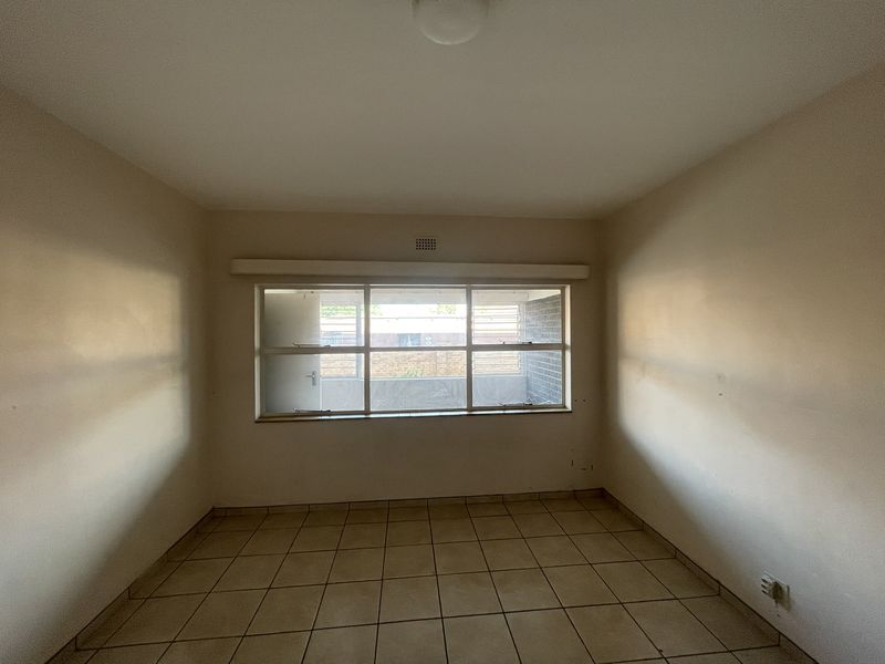 An empty bedroom featuring neutral tiled flooring and a large window, providing a blank canvas for personalization.