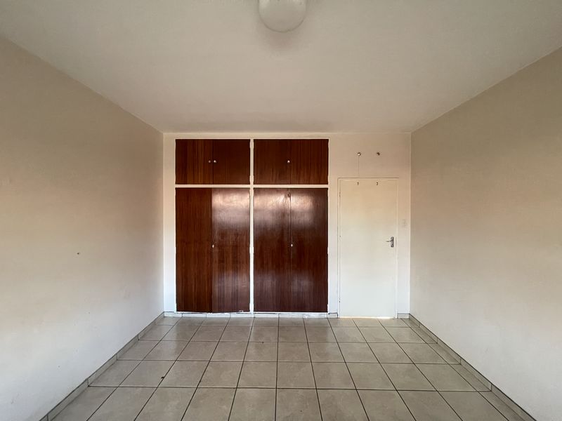 An empty bedroom featuring tiled flooring and built-in wooden cupboards, offering a blank canvas for renovation or interior design updates.