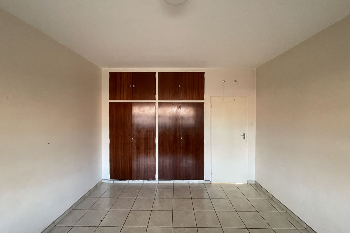 An empty bedroom featuring tiled flooring and built-in wooden cupboards, offering a blank canvas for renovation or interior design updates.