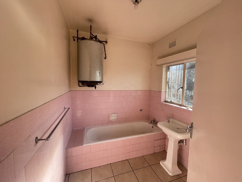 A dated bathroom featuring a built-in bathtub, pedestal basin, and exposed electric water heater, requiring modernization of finishes and fixtures.