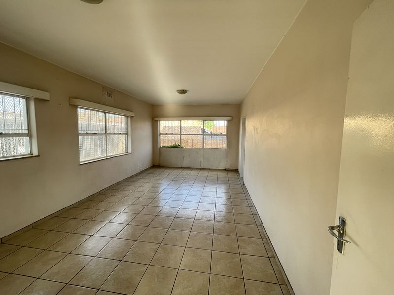 An empty, neutrally painted living area featuring tiled flooring and large windows with security bars, offering a blank canvas for potential renovation.