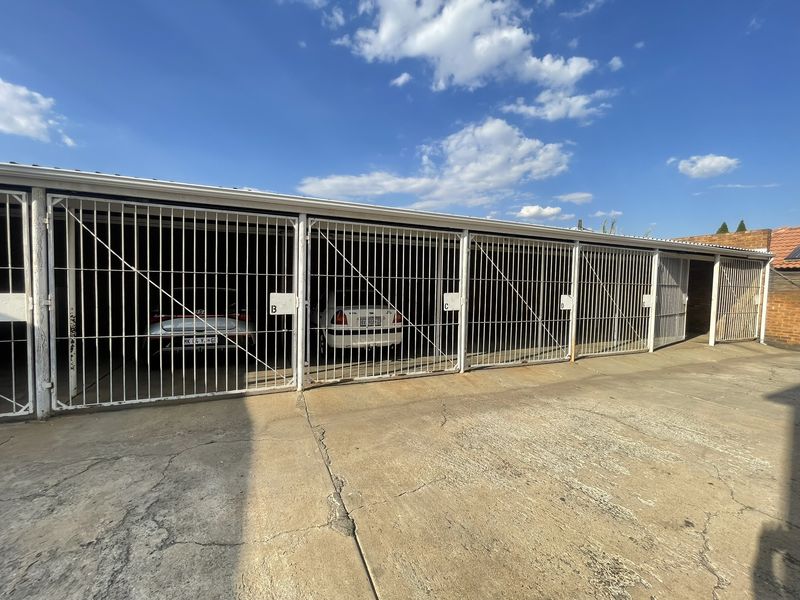 A row of secure, gated garage parking bays with a concrete driveway, showing signs of wear and tear.