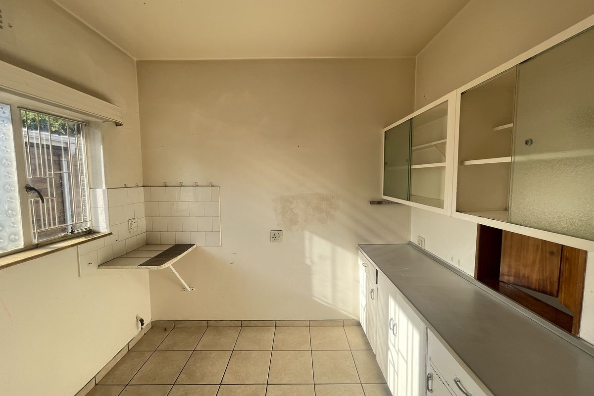 An empty, dated kitchen featuring original built-in cabinetry, tiled flooring, and a tiled splashback, offering a blank canvas for renovation.