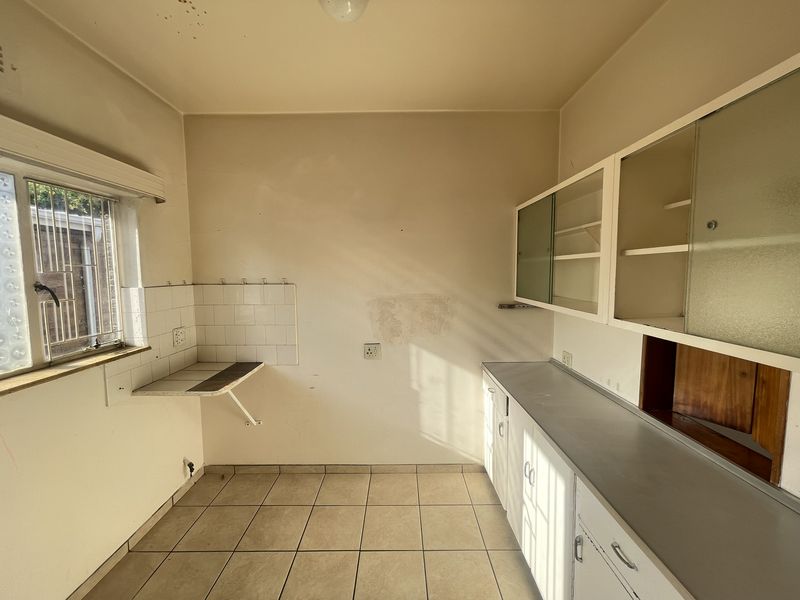 An empty, dated kitchen featuring original built-in cabinetry, tiled flooring, and a tiled splashback, offering a blank canvas for renovation.