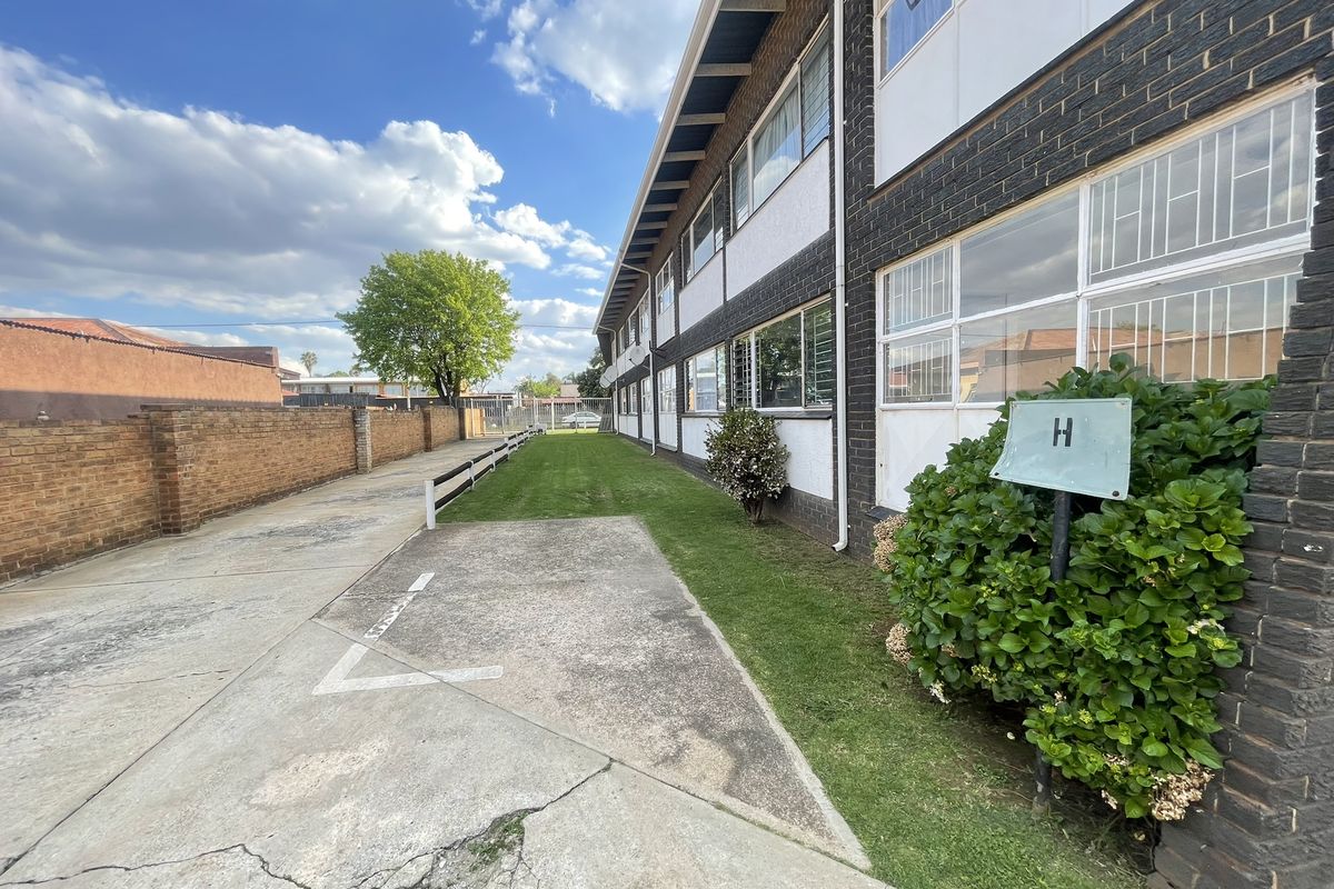 Exterior view of the apartment building featuring a brick facade, concrete driveway, and landscaped lawn area.