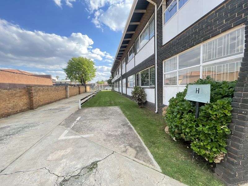 Exterior view of the apartment building featuring a brick facade, concrete driveway, and landscaped lawn area.