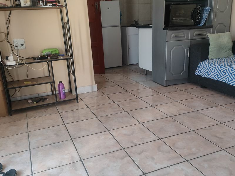 An open-plan living and kitchen area featuring ceramic tiled flooring and basic built-in cabinetry, requiring cosmetic updates to improve the overall aesthetic.