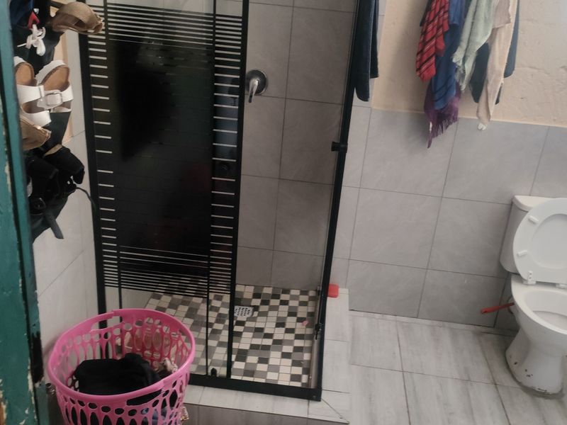 A functional bathroom featuring a shower enclosure with a black frame, a standard toilet, and tiled finishes throughout.