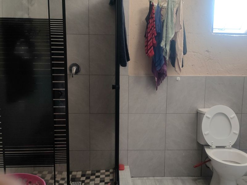 A functional bathroom featuring a shower enclosure and toilet, with tiled walls and flooring. The space would benefit from cosmetic updates and repairs.