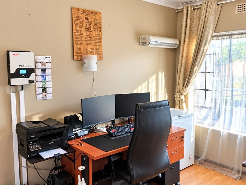 A functional home office space featuring laminate flooring, a wall-mounted solar inverter, and a split-system air conditioner for climate control.