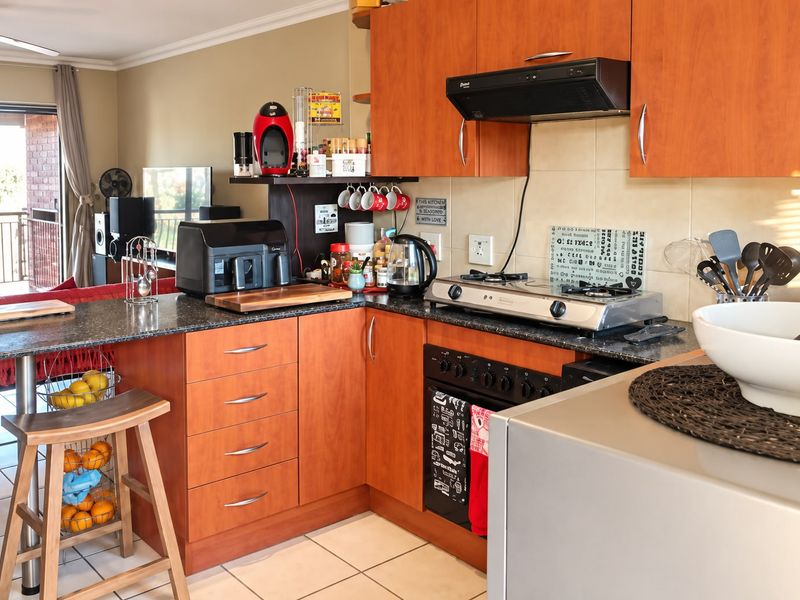 Open-plan kitchen featuring wood-finish cabinetry, granite countertops, gas hob, and breakfast bar, seamlessly flowing into the adjacent living area.