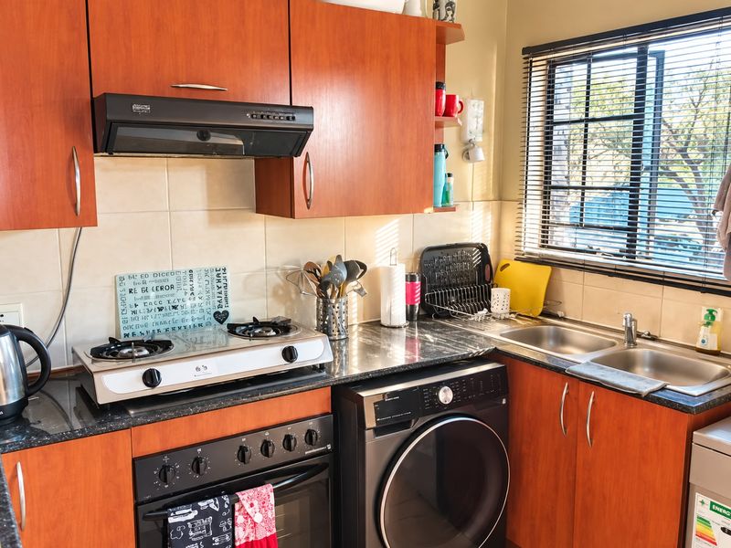 A functional kitchen featuring wood-finish cabinetry, granite countertops, a double stainless steel sink, and integrated cooking appliances with a tiled backsplash.