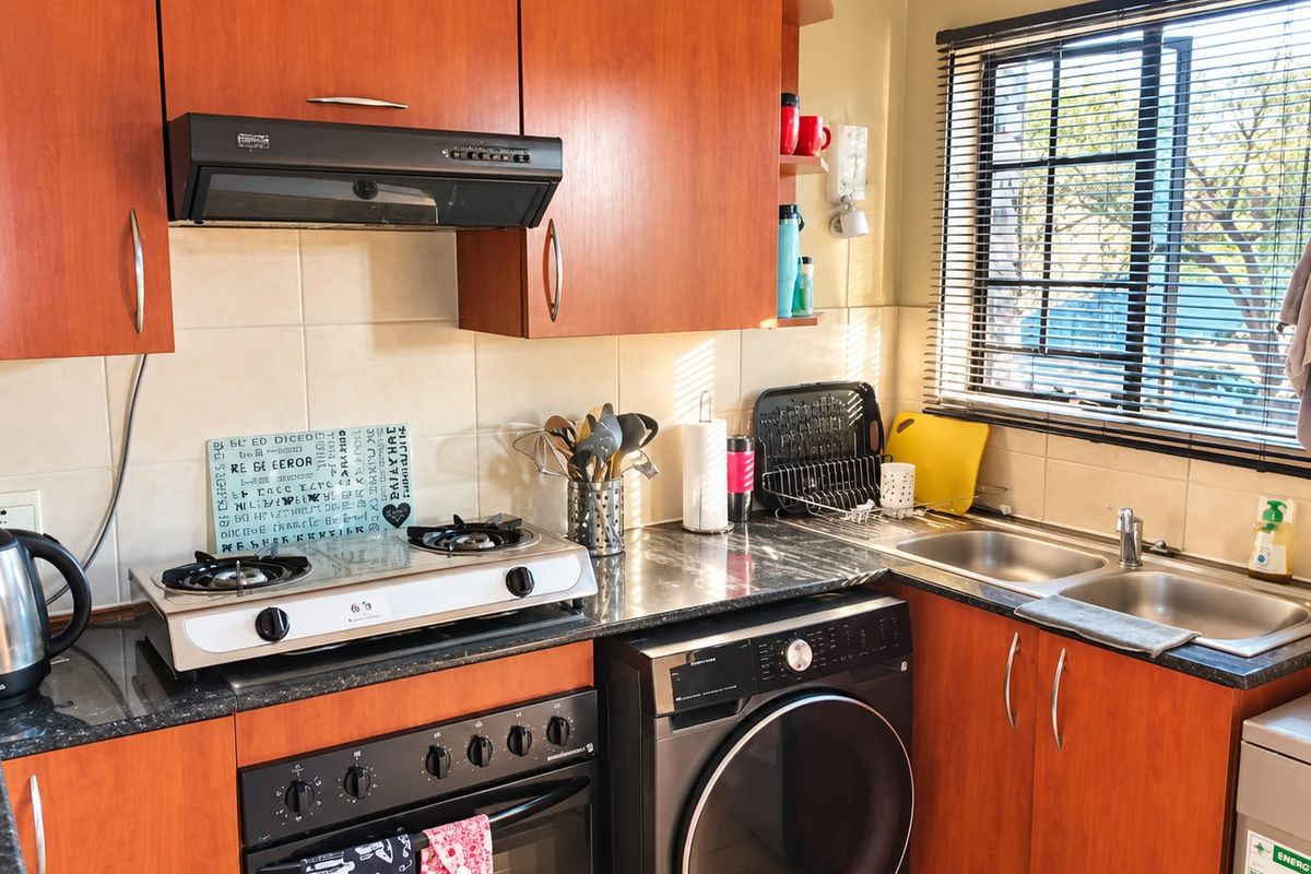 A functional kitchen featuring wood-finish cabinetry, granite countertops, a double stainless steel sink, and integrated cooking appliances with a tiled backsplash.