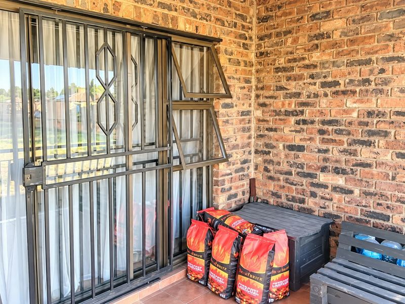 A covered patio area featuring exposed brick walls, tiled flooring, and secure aluminium window and door frames.