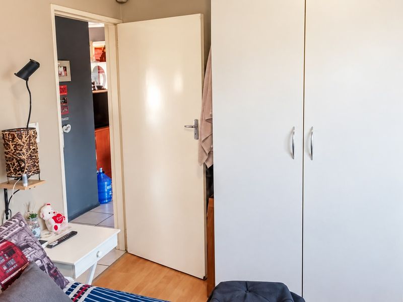 A bedroom featuring laminate flooring and a white built-in wardrobe, with a doorway leading to an adjacent living area.