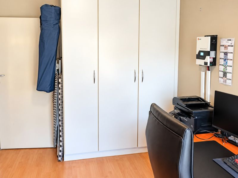 A functional home office space featuring laminate flooring and a large built-in wardrobe for storage, equipped with a wall-mounted solar inverter.